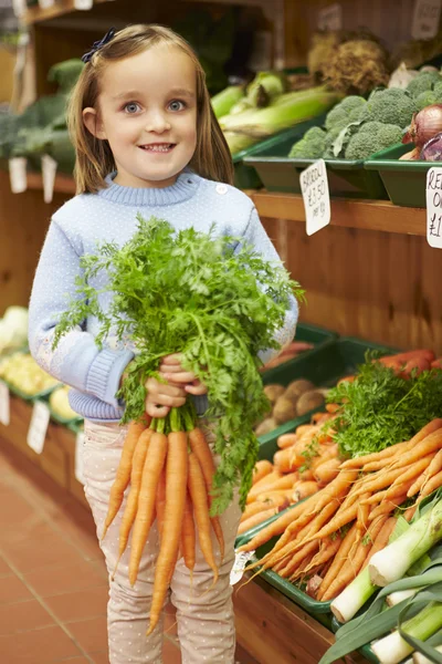 Jong meisje houden bos van wortelen in Boerderijwinkel — Stockfoto
