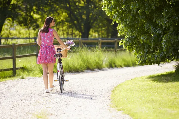 Vue arrière comme femme pousse le vélo le long de la voie de campagne — Photo