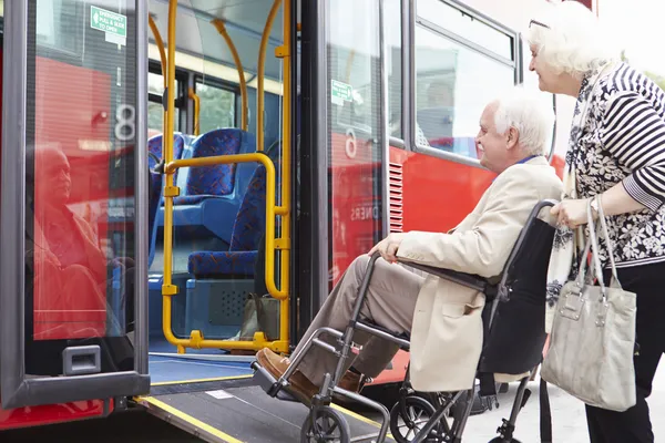 Senior coppia imbarco autobus utilizzando rampa di accesso per sedie a rotelle — Foto Stock