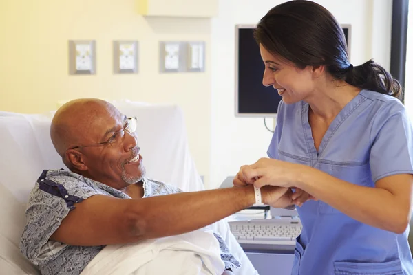 Enfermera poniendo pulsera en paciente masculino mayor en el hospital —  Fotos de Stock