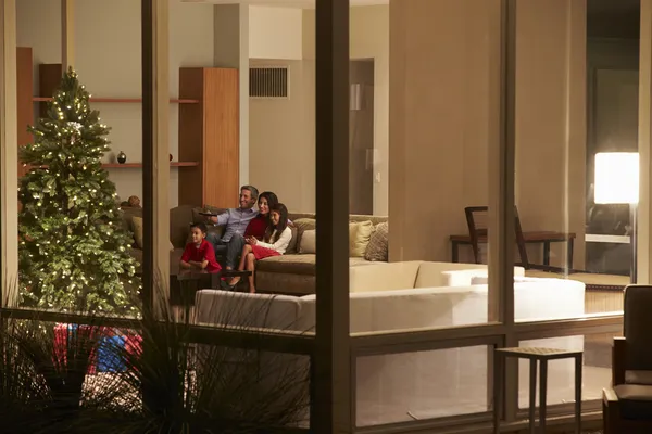 Familia viendo la televisión navideña en casa vista desde fuera — Foto de Stock