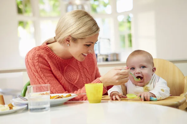 Mamma utfodring baby sitter i barnstol vid måltiderna — Stockfoto