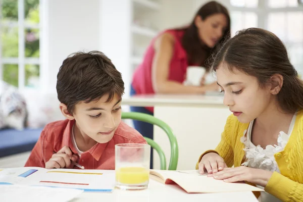 Děti dělat domácí úkoly, jako matka používá notebook v pozadí — Stock fotografie