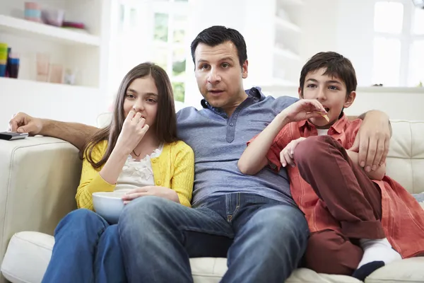 Padre e hijos sentados en un sofá viendo televisión juntos — Foto de Stock