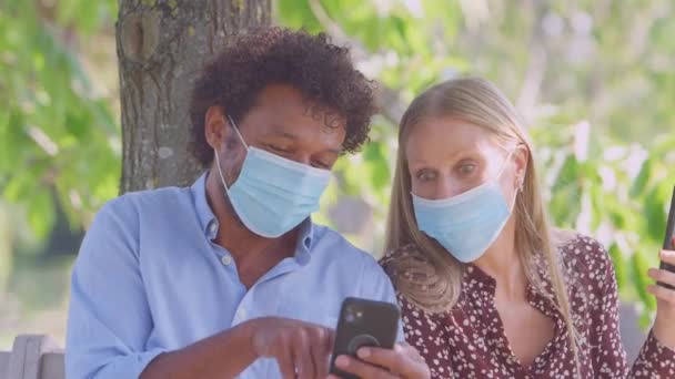 Par Iført Masker Møde Udendørs Park Sundhedspandemi Ser Mobiltelefoner – Stock-video