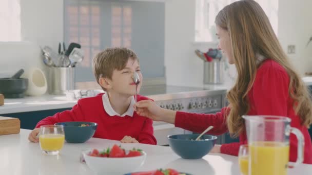 キッチンで制服を着た兄と妹が朝食時に鼻からスプーンをぶら下げるのが楽しい — ストック動画