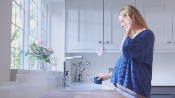 笑顔妊娠中の女性がキッチンウィンドウで立ちます 胃に触れる — ストック動画