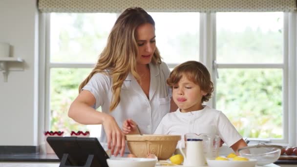 デジタルタブレット上のレシピに続いて自宅で台所でパジャマ焼きで母と息子 — ストック動画