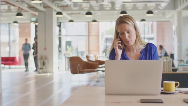 同僚とのモダンなオープンプランオフィスで電話でデスクに座っているビジネスマン女性 — ストック動画