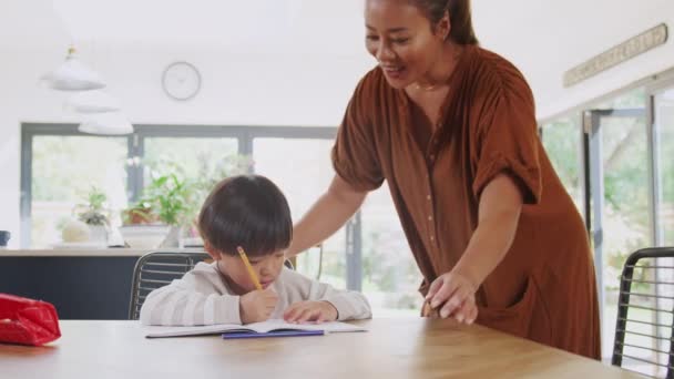 亚洲母亲帮助儿子在家上学在餐桌边工作在厨房写书 — 图库视频影像