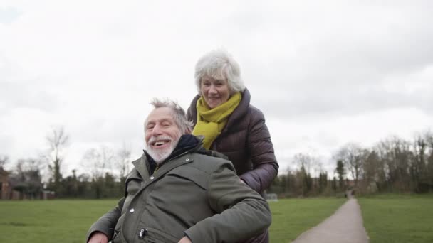 Senior Woman Pushing Senior Man Wheelchair Outdoors Fall Winter Park — Stock video