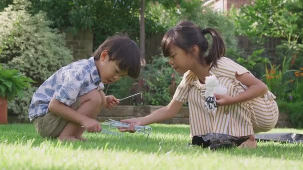 夏のキャンプ旅行の前にテントのペグで遊ぶ自宅の庭でアジアの兄弟姉妹 — ストック動画