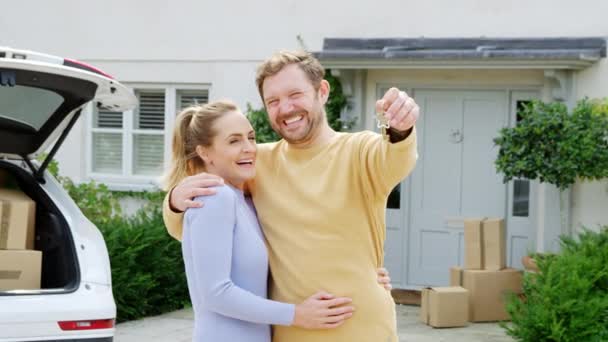 移動中の日に新しい家の外に鍵を保持するカップルの肖像車から箱をアンロード — ストック動画