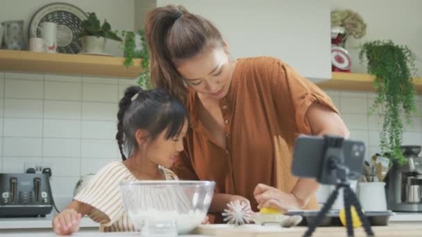 亚洲母亲和女儿在厨房里烘焙蛋糕 一边在手机上发短信 — 图库视频影像