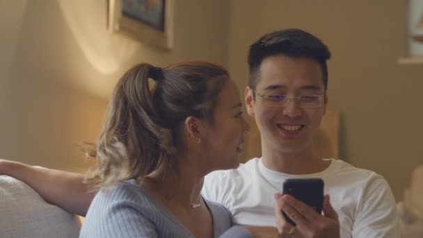Gülümseyen Asyalı Çift Akşam Birlikte Cep Telefonuna Bakarken Koltukta Dinleniyor — Stok video