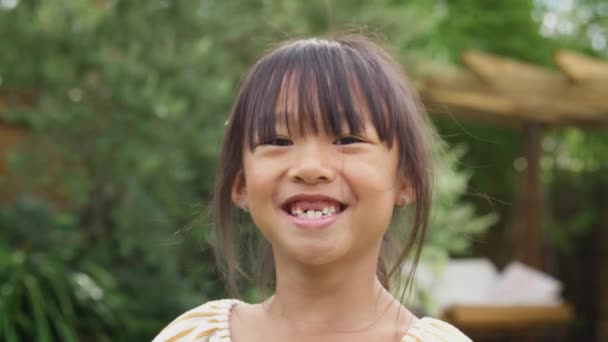 行方不明の前歯を持つ笑顔アジアの女の子の肖像 自宅で庭で楽しみを持っています — ストック動画