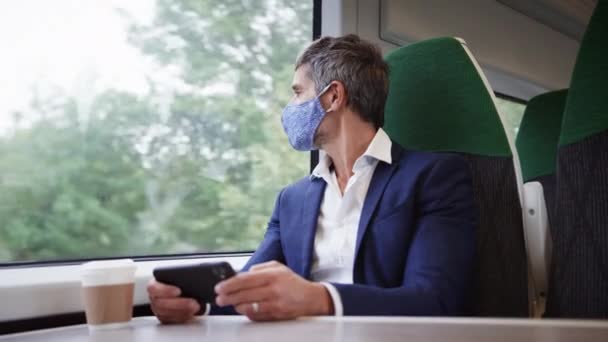健康の流行の間にPpeフェイスマスクを身に着けている携帯電話を使用して電車の中でビジネスマン — ストック動画