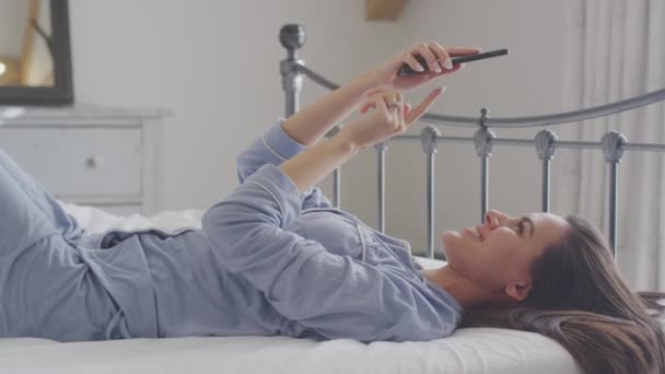 穿着睡衣的女人躺在床上 在手机上自作主张 — 图库视频影像