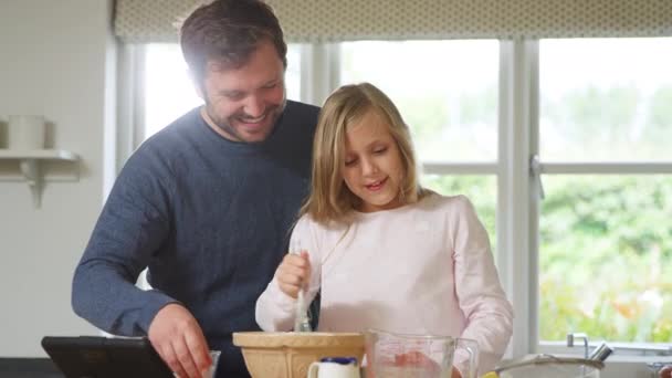 デジタルタブレットでレシピに続いて自宅でキッチンでパジャマ焼きの父と娘 — ストック動画