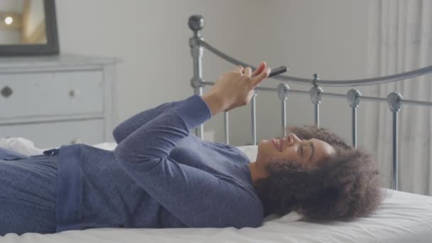 Glimlachende Jonge Vrouw Liggend Bed Met Mobiele Telefoon Dragen Pyjama — Stockvideo