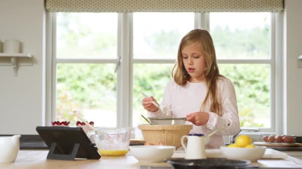 デジタルタブレットでレシピに続く自宅のキッチンでパジャマ焼きを身に着けている女の子 — ストック動画
