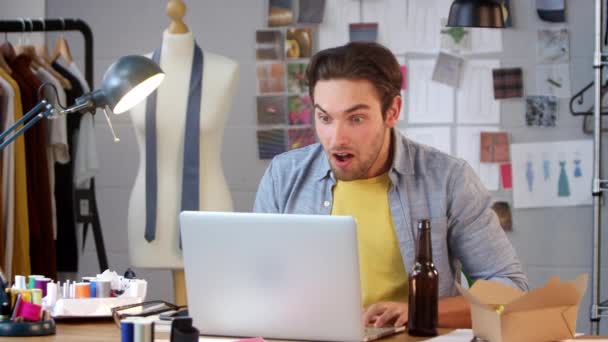 男性时装设计师 带着啤酒瓶 一边在笔记本电脑上观看运动 一边在工作室里庆祝 — 图库视频影像