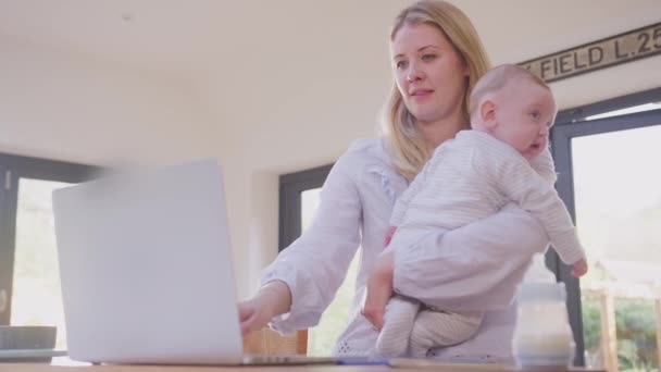 工作的母亲在家里用笔记本电脑 抱着小儿子抱着肩膀 动作缓慢 — 图库视频影像