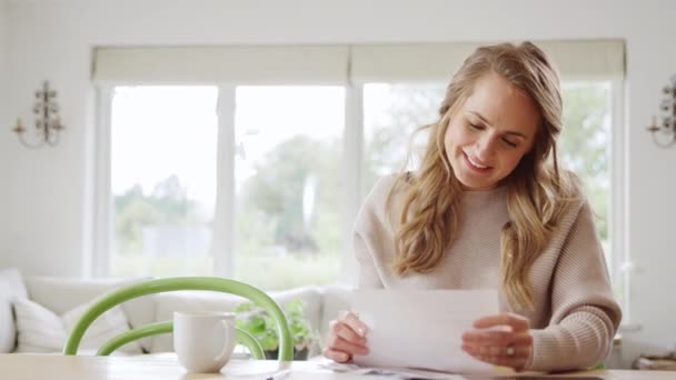 笑顔の女性が自宅でテーブルに座っている国内の財務状況を確認良いニュースで手紙を開く — ストック動画