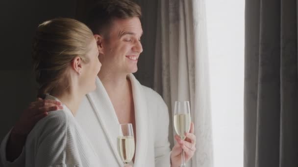 情侣们穿着浴袍 站在浪漫的酒店旁边 站在敞开的窗帘旁 喝着一杯香槟 — 图库视频影像