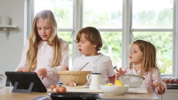 穿着睡衣在厨房做松饼的孩子们在家中跟随数码桌面上的食谱 — 图库视频影像