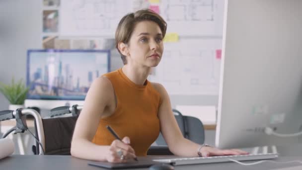在办公室轮椅上工作的残疾女性建筑师使用图形表格在台式计算机上工作 — 图库视频影像