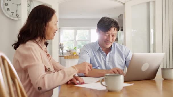 成熟したアジアのカップルは 家庭の請求書や財政を整理するためにラップトップを使用して自宅でテーブルに座って スローモーションで撮影 — ストック動画
