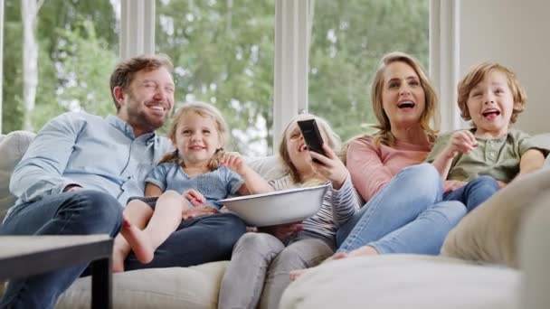 Οικογένεια Κάθεται Στον Καναπέ Στο Σπίτι Γελώντας Και Βλέποντας Τηλεόραση — Αρχείο Βίντεο