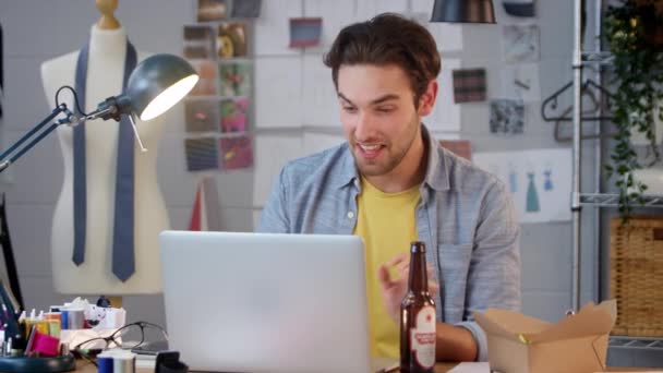 ビールのボトルでファッションビジネスの男性の所有者スタジオでノートパソコンでビデオ通話を作る — ストック動画