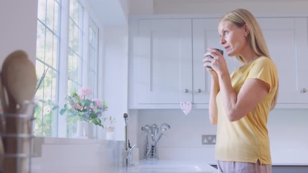 熟女自宅で熱い飲み物がキッチンの窓そばに立つ — ストック動画