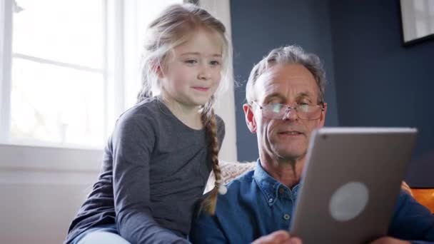 祖父と孫娘で家に座っていますアームチェアで一緒にデジタルタブレットを使用して — ストック動画