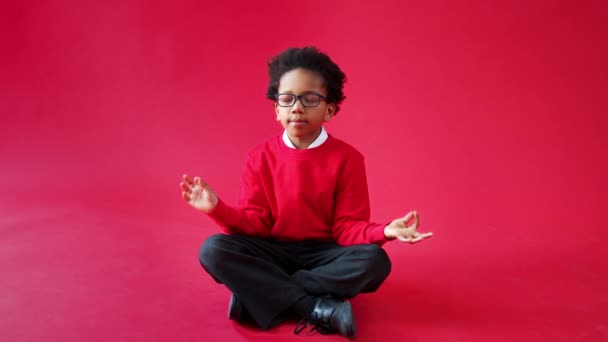 男子小学生服を着て制服座って瞑想に対して赤いスタジオの背景 ショットでスローモーション — ストック動画