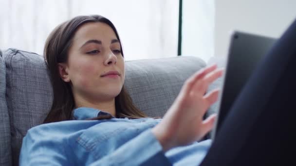 Jovem Relaxada Casa Deitada Sofá Olhando Para Tablet Digital Filmada — Vídeo de Stock