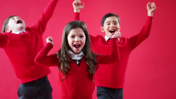 Groep Enthousiaste Basisscholieren Met Uniform Gejuich Camera Tegen Rode Studioachtergrond — Stockvideo