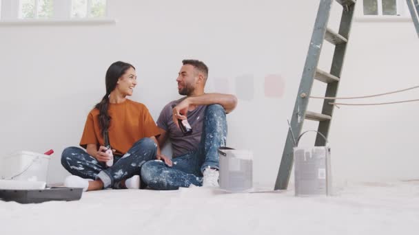 彼らは一緒に新しい家で部屋を飾るようにカップルは 壁に座ってビールを飲む休憩を取ります スローモーションで撮影 — ストック動画
