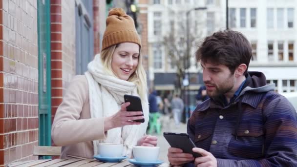 情侣们正坐在繁忙的城市大街上的咖啡店外 看着数码设备 慢镜头拍摄 — 图库视频影像