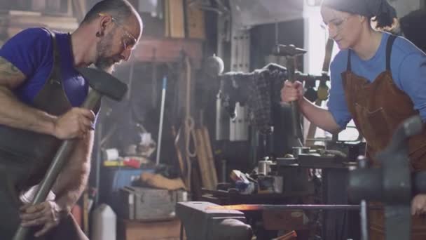 男性と女性の鍛冶屋が一緒にアンビル上の金属細工の赤いホットピースをハンマー スローモーションで撮影 — ストック動画