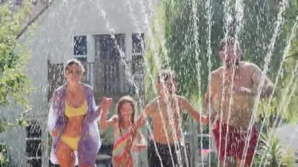 Family Wearing Swimming Costumes Having Water Running Water Garden Sprinkler — Stock Video