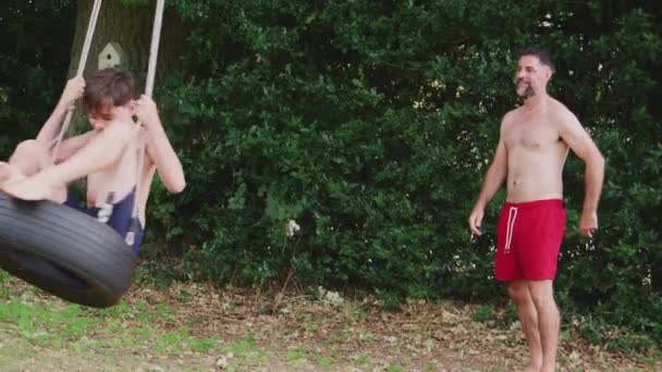 Father Wearing Swimming Costume Pushing Son Tire Swing Summer Garden — Stock Video