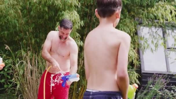 夏天花园里穿着泳衣 拿着水枪打水仗的家庭 动作缓慢 — 图库视频影像