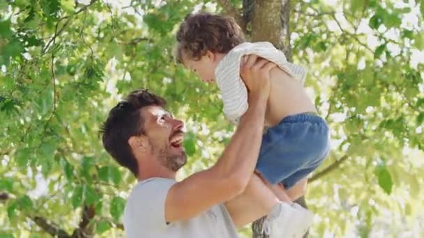 愛する父とともに楽しいです若い息子で公園で彼を空中で持ち上げる前に彼を抱きしめる スローモーションで撮影 — ストック動画