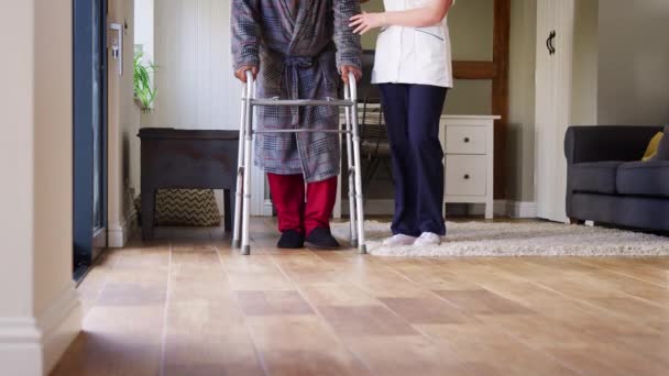 ウォーキングフレームを使用してガウンを身に着けている高齢者のクローズアップは 女性介護労働者によって助けられて スローモーションで撮影 — ストック動画