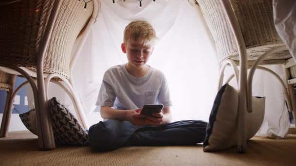 少年はデンやキャンプに座って 彼は自宅で携帯電話で遊んで作られています スローモーションで撮影 — ストック動画