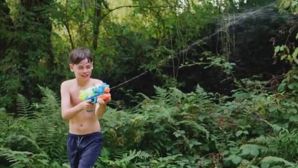 Мальчик Купальнике Водяным Пистолетом Водной Борьбы Летнем Саду Снято Замедленной — стоковое видео