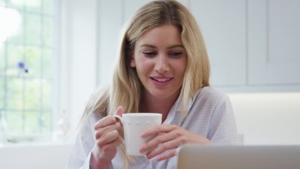 Woman Wearing Pyjamas Kitchen Home Using Laptop Whilst Eating Breakfast — Stockvideo